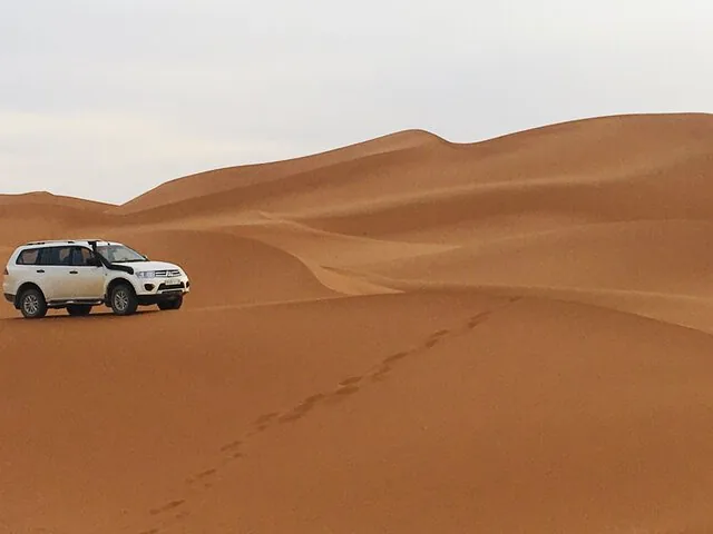White 4x4 vehicle parked on a large sand dune in the desert