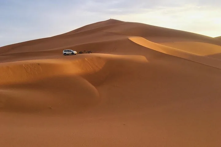 4x4 vehicle parked near the base of a massive sand dune at sunset